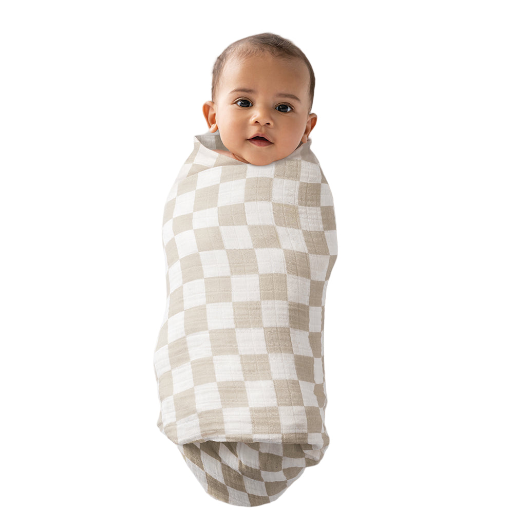 Baby wrapped in a green and white checkered swaddle on a plain background