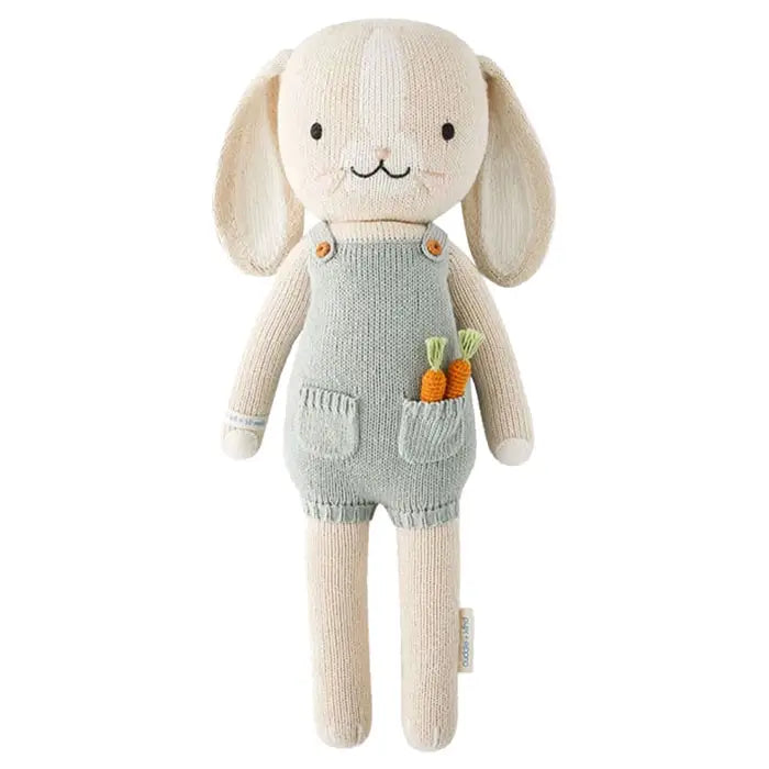 Knitted toy rabbit with overalls and carrots on a white background