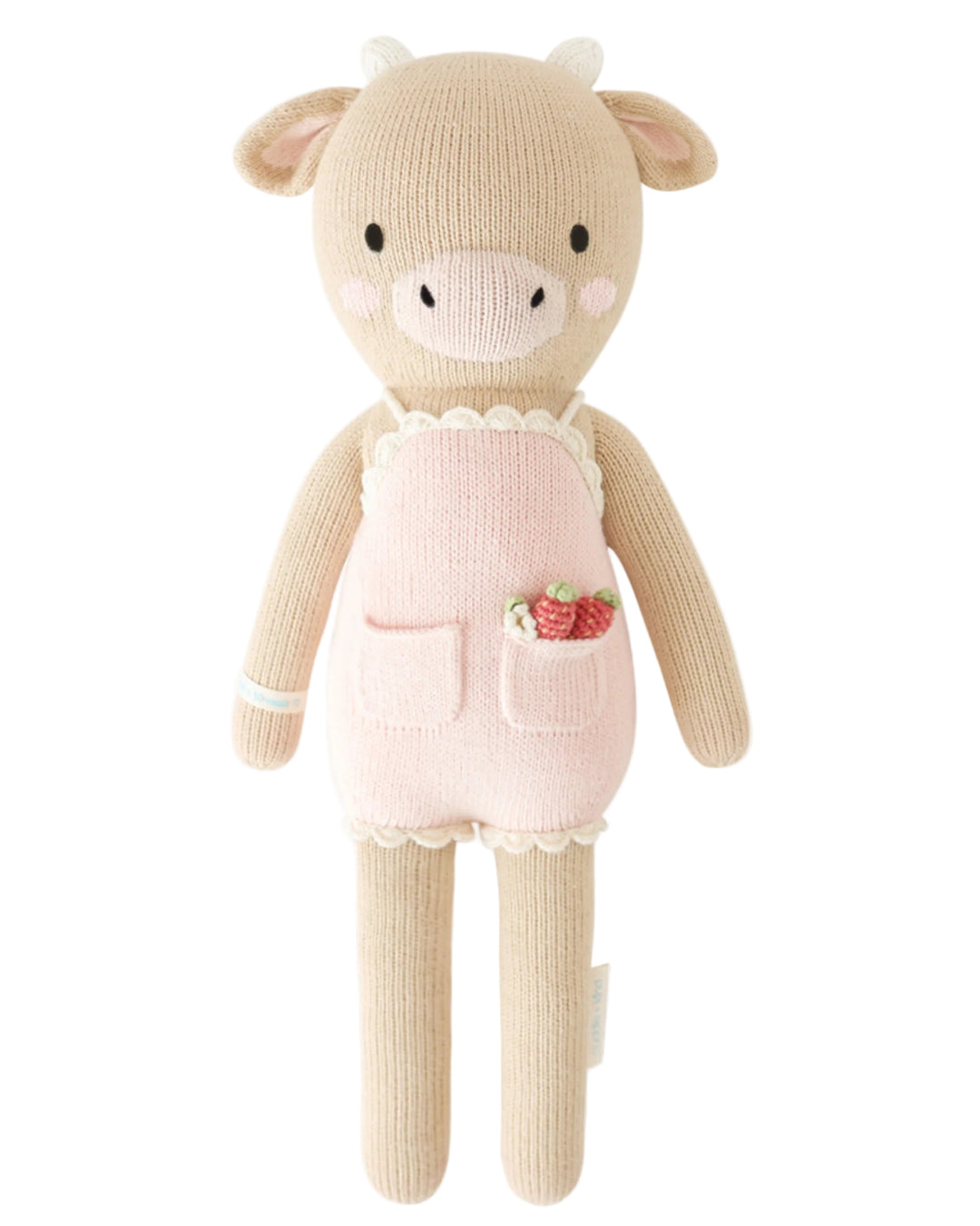 Knitted toy cow wearing a pink outfit with a strawberry design on a white background